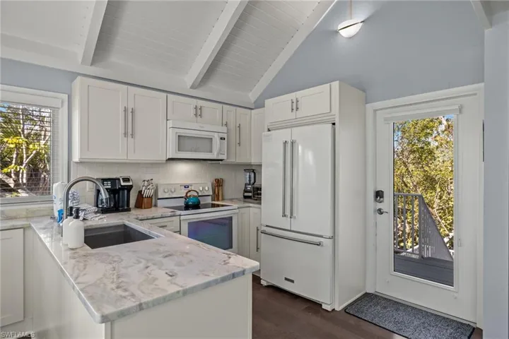 Kitchen with light stone countertops, dark hardwood / wood-style floors, white appliances, decorative backsplash, and white cabinets