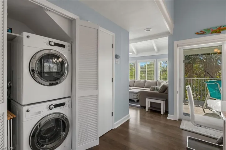 Clothes washing area with dark hardwood / wood-style flooring and stacked washer and clothes dryer
