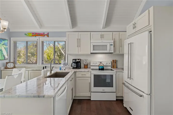 Kitchen with light stone countertops, backsplash, white appliances, sink, and white cabinets