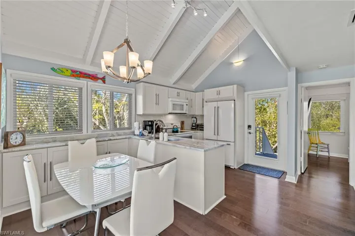 Kitchen featuring white appliances, decorative light fixtures, an inviting chandelier, white cabinets, and a center island