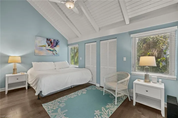 Bedroom featuring ceiling fan, dark wood-type flooring, wooden ceiling, vaulted ceiling with beams, and multiple closets