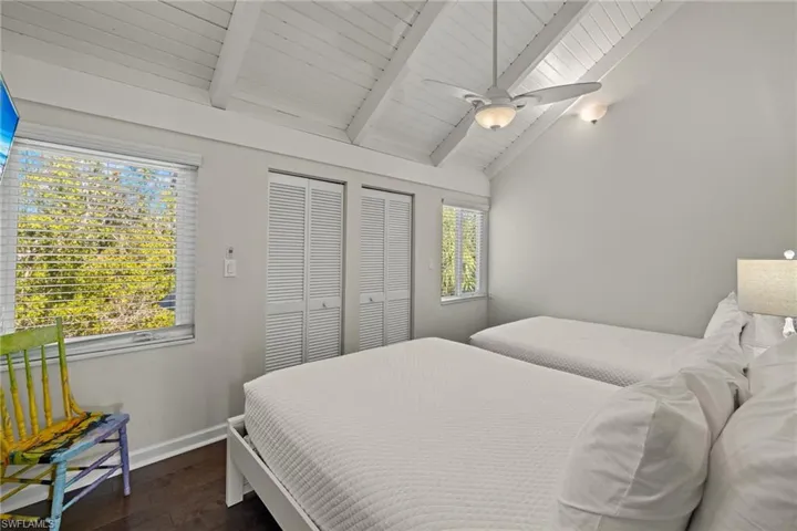 Bedroom with multiple windows, ceiling fan, lofted ceiling with beams, and dark hardwood / wood-style floors