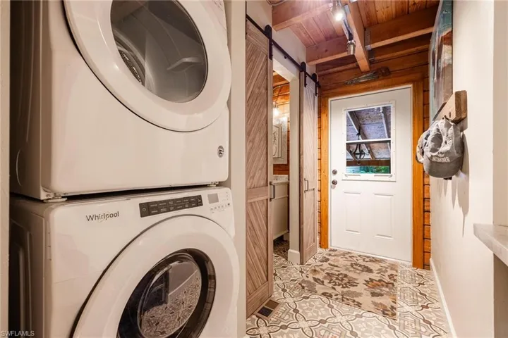 Washroom featuring wooden walls, a barn door, stacked washer and clothes dryer, wooden ceiling, and light tile patterned floors