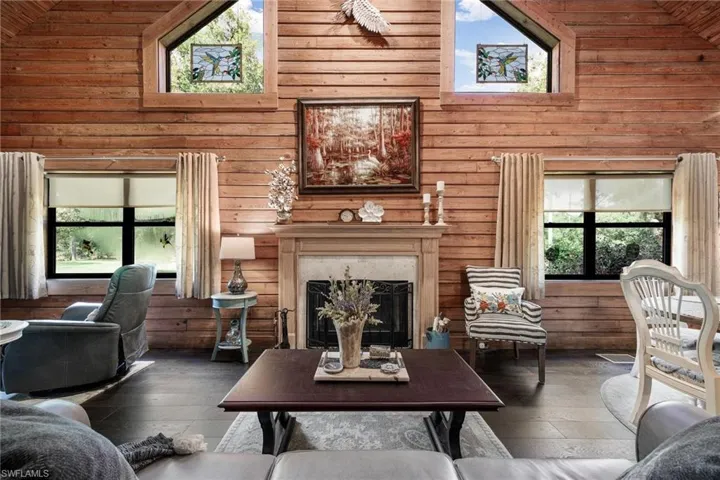 Living room featuring a fireplace, wooden walls, high vaulted ceiling, and dark hardwood / wood-style floors