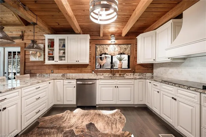 Kitchen with custom exhaust hood, stainless steel dishwasher, hanging light fixtures, and beamed ceiling