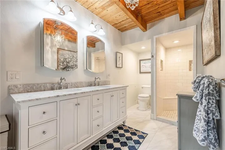 Downstairs Master Bathroom with tiled shower, dual bowl vanity, tile patterned floors, wood ceiling, and toilet
