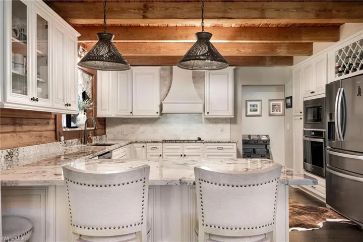 Kitchen featuring backsplash, custom range hood, beam ceiling, appliances with stainless steel finishes, and decorative light fixtures