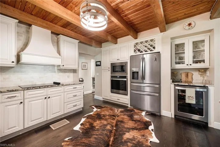 Kitchen with custom range hood, stainless steel appliances, decorative backsplash, wooden ceiling, and beverage cooler