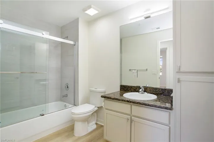 Bathroom with vanity, wood finished floors, toilet, and enclosed tub / shower combo