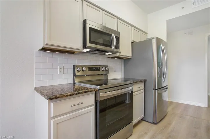 Kitchen featuring appliances with stainless steel finishes, light wood-style floors, tasteful backsplash, dark stone countertops, and baseboards