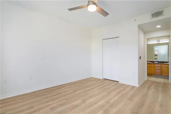 Unfurnished bedroom with light wood-type flooring, baseboards, a closet, a ceiling fan, and connected bathroom