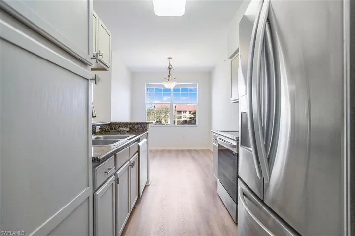 Kitchen with appliances with stainless steel finishes, light wood-style floors, dark countertops, gray cabinets, and pendant lighting