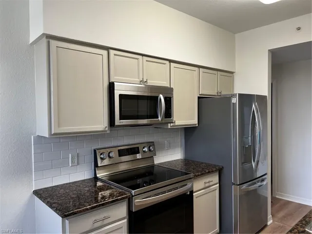 Kitchen featuring stainless steel microwave, stove, decorative backsplash, and wood finished floors