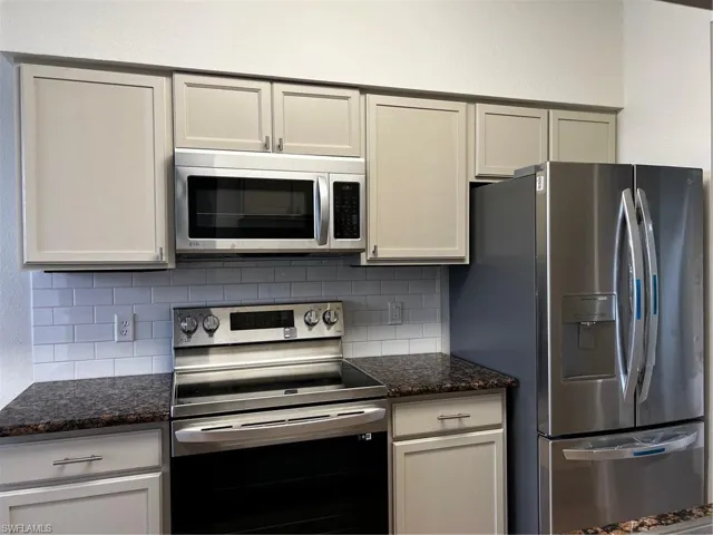Kitchen featuring refrigerator, range, tasteful backsplash, and dark stone counters