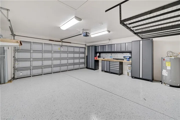 Multi-car garage featuring epoxy-coated flooring, built-in metal cabinetry, an integrated workbench, overhead ceiling storage racks, and fluorescent lighting