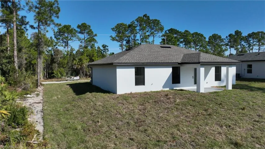 Rear view of house with a lawn, a patio, stucco siding, and a shingled roof