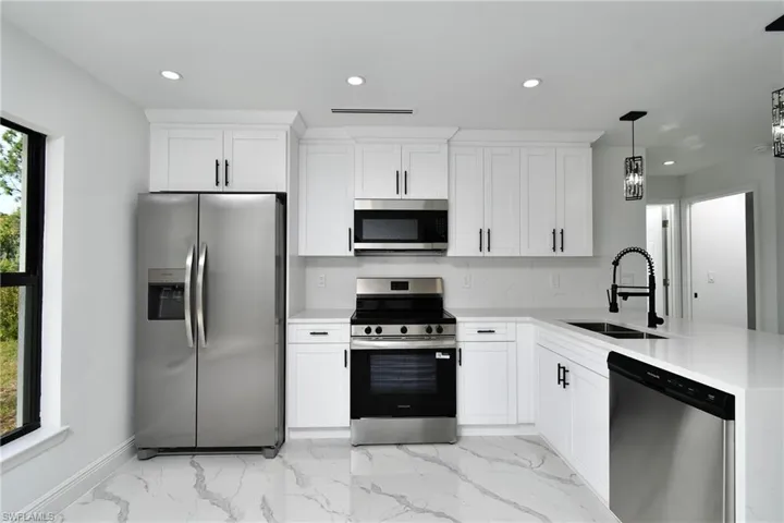 Kitchen with stainless steel appliances, hanging light fixtures, light stone countertops, and white cabinets