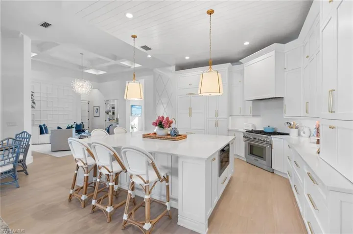 Kitchen featuring coffered ceiling, a kitchen breakfast bar, white cabinets, stainless steel appliances, and light wood-style floors