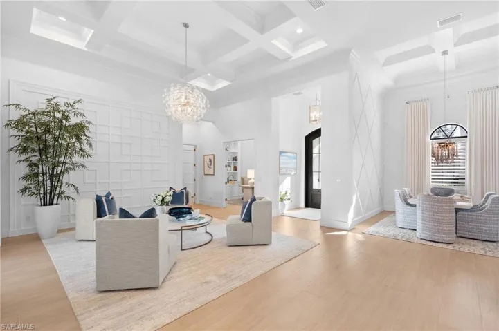 Living room with suspended lighting, coffered ceiling, healthy amount of natural light, crown molding, and light wood-style flooring