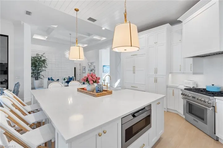Kitchen with coffered ceiling, white cabinetry, a kitchen bar, stainless steel appliances, and pendant lighting