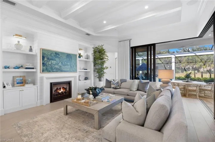 Living area with built in features, a warm lit fireplace, light wood-style floors, crown molding, and recessed lighting