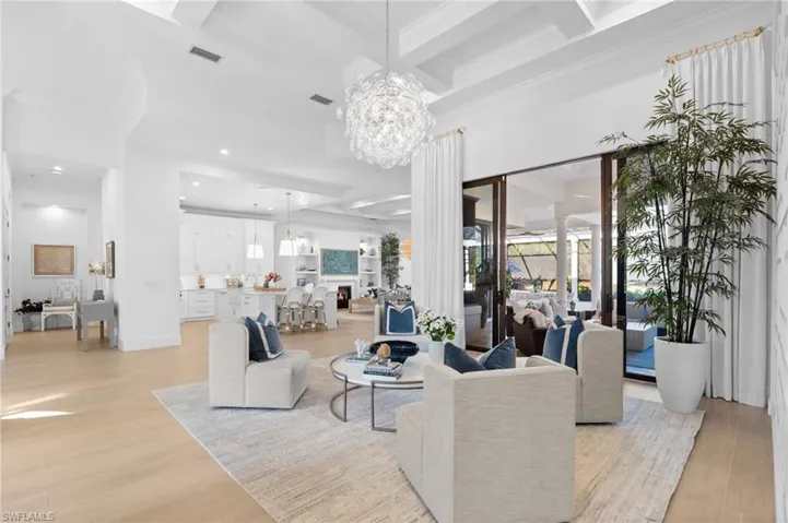 Living room with coffered ceiling, light wood-type flooring, a chandelier, and crown molding