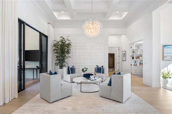 Living area with suspended lighting, coffered ceiling, wood finished floors, and ornamental molding