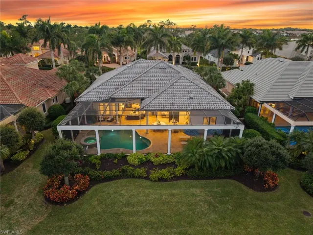 Back of house at dusk with a sunroom, a lawn, an outdoor pool, an in-ground hot tub, and a tiled roof