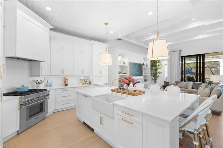 Kitchen featuring a breakfast bar area, high end stainless steel range, white cabinetry, hanging light fixtures, and an island with sink
