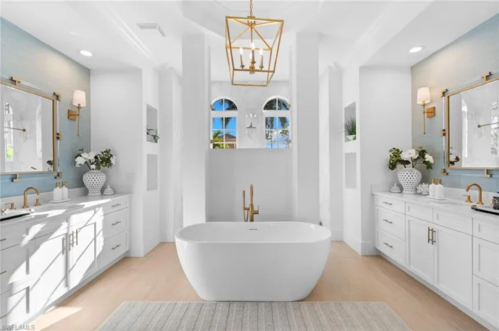 Full bath with two vanities, a freestanding tub, light wood-type flooring, and a chandelier