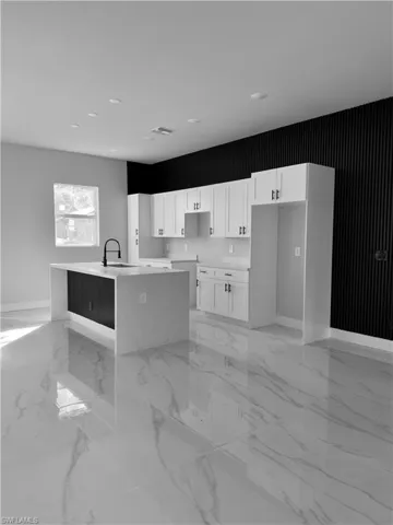 Kitchen with light marble finish floors, white cabinetry, light stone countertops, and a center island with sink