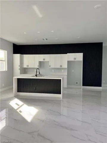 Kitchen featuring white cabinets, a kitchen island with sink, light marble finish flooring, and light stone counters