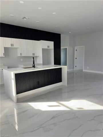 Kitchen with light stone countertops, white cabinets, a kitchen island with sink, and light marble finish floors