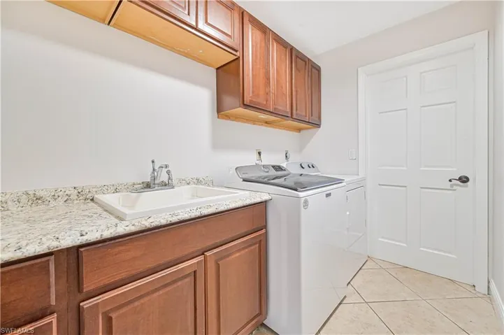 Laundry area featuring cabinet space, light tile patterned flooring, and washing machine and dryer