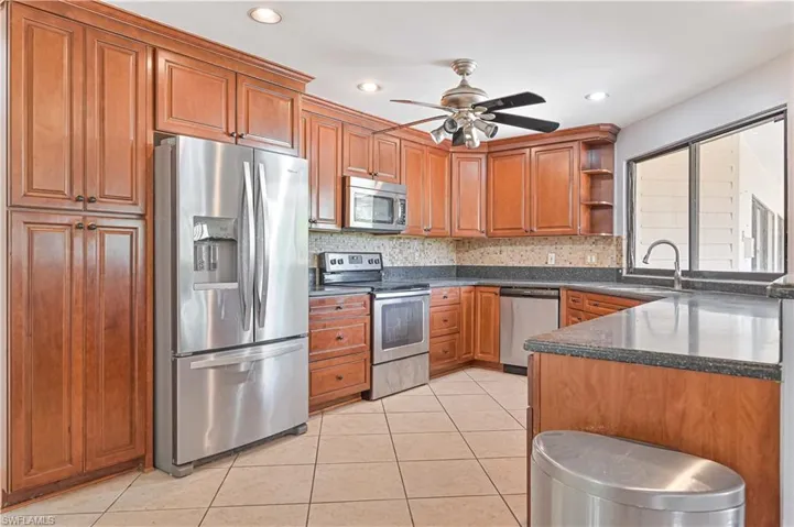 Kitchen with appliances with stainless steel finishes, brown cabinets, open shelves, dark stone counters, and backsplash