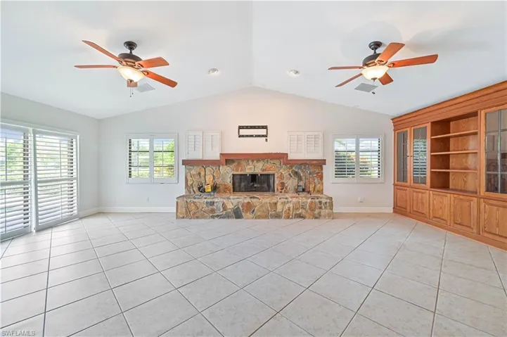 Unfurnished living room with ceiling fan, a fireplace, built in shelves, vaulted ceiling, and light tile patterned flooring