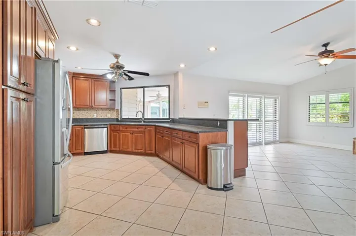 Kitchen with brown cabinetry, a ceiling fan, a peninsula, appliances with stainless steel finishes, and light tile patterned floors