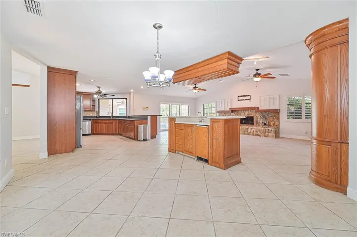 Kitchen featuring a chandelier, open floor plan, pendant lighting, a stone fireplace, and brown cabinetry