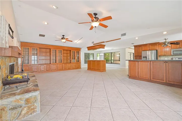 Unfurnished living room featuring a ceiling fan, recessed lighting, light tile patterned flooring, a fireplace with raised hearth, and built in shelves