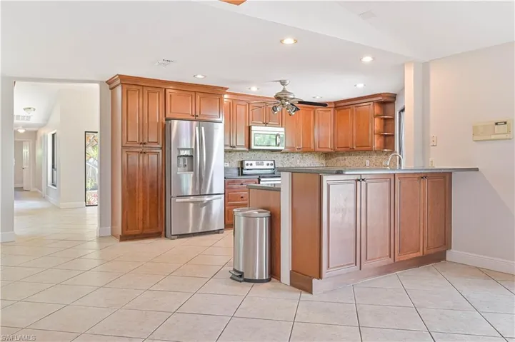 Kitchen with brown cabinets, stainless steel appliances, a peninsula, recessed lighting, and light tile patterned floors