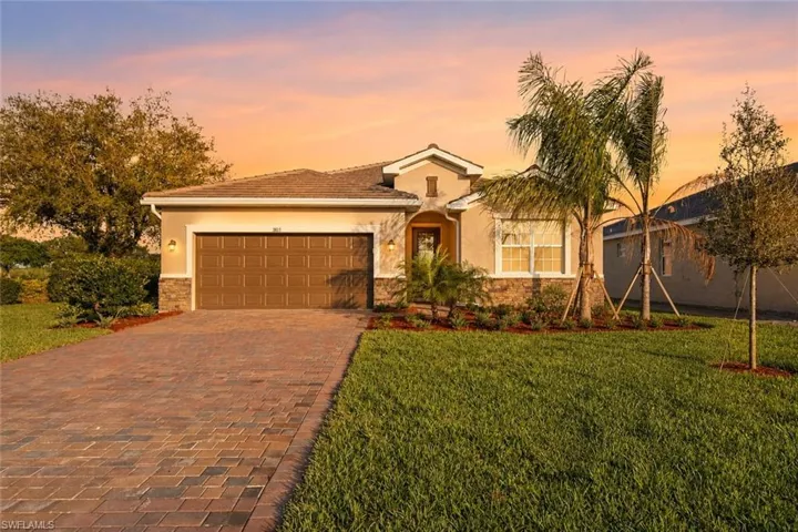Stucco exterior with stone accents, paver driveway, attached two-car garage, and mature landscaping