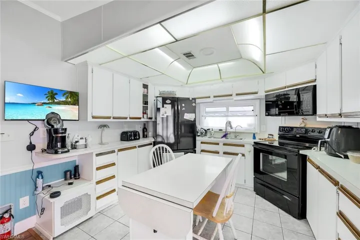 Kitchen with black appliances, white cabinetry, and light tile patterned floors
