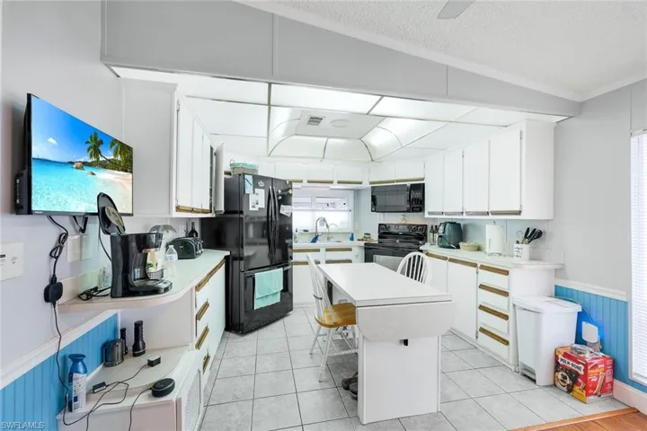 Kitchen with white cabinets, light tile patterned floors, a textured ceiling, black appliances, and a center island