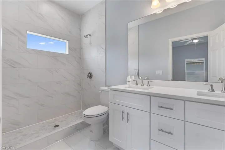 Full bath featuring double vanity, a tile shower, a ceiling fan, and light marble finish floors