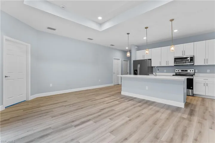 Kitchen with stainless steel appliances, an island with sink, decorative light fixtures, white cabinets, and a tray ceiling