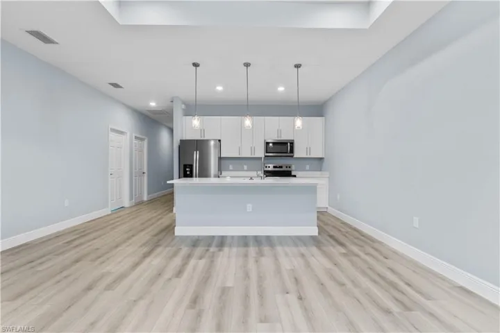 Kitchen featuring a center island with sink, stainless steel appliances, pendant lighting, white cabinets, and light wood-style flooring