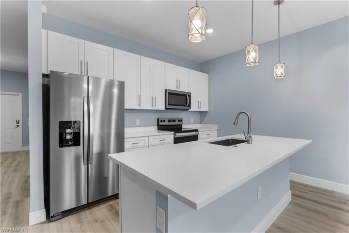 Kitchen with stainless steel appliances, white cabinets, decorative light fixtures, a center island with sink, and light wood-style floors