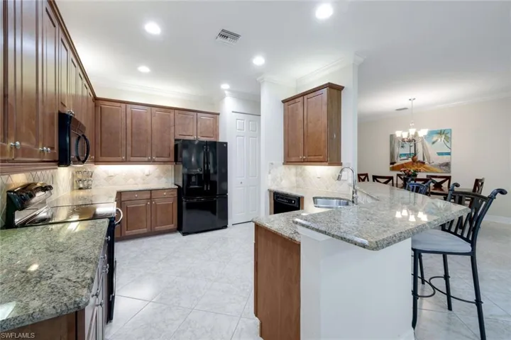 Open kitchen with wood cabinetry and granite countertops, a separate pantry (not shown), lots of counter space and storage, a breakfast bar and an adjoining, dedicated eat-in kitchen area.