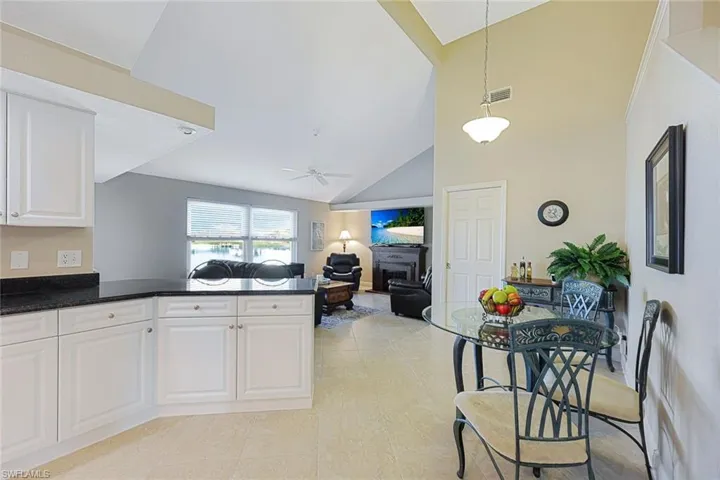 Kitchen featuring ceiling fan, white cabinetry, a fireplace, and high vaulted ceiling