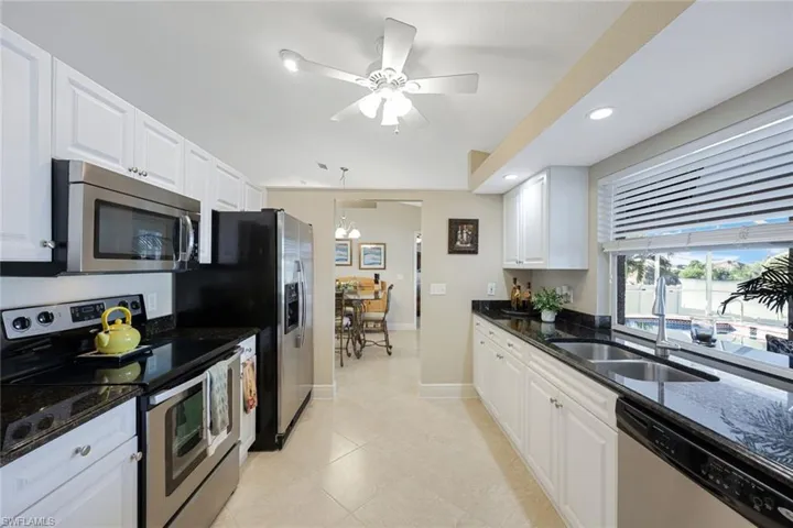 Kitchen featuring white cabinetry, sink, stainless steel appliances, dark stone countertops, and pendant lighting
